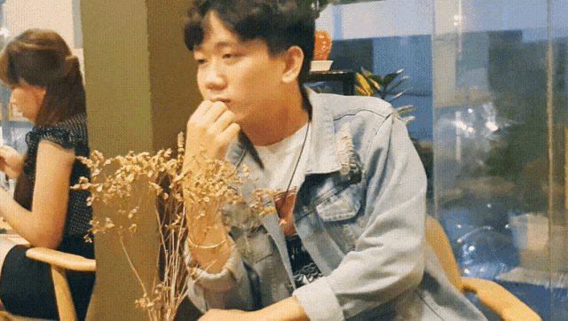 a young man in a denim jacket sits in a chair