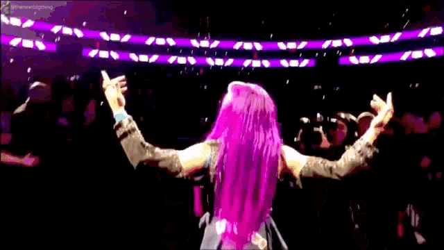 a woman with pink hair is standing in a ring while a man takes a picture .
