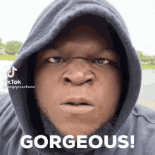 a man wearing a hooded sweatshirt is making a funny face and saying gorgeous .