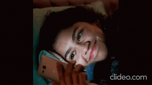 a woman laying on a bed looking at her phone with clideo.com written on the bottom