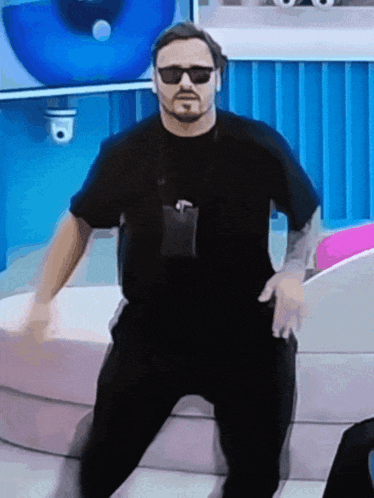 a man wearing sunglasses and a lanyard is dancing on a couch
