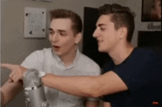 two men are standing next to each other and one is pointing at the camera .