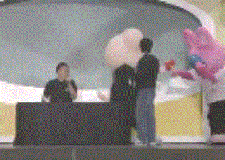 a group of people standing around a table with a pink mascot standing in front of them .