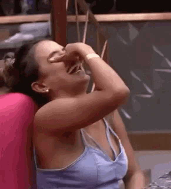 a woman in a blue tank top is laughing with her hand over her nose .