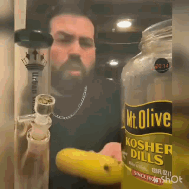 a man smoking a bong next to a bottle of kosher dill
