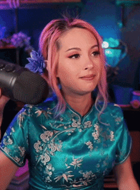 a woman with pink hair is standing in front of a microphone wearing a blue dress
