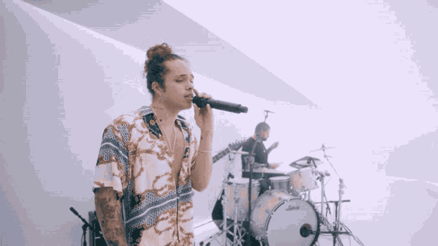 a man singing into a microphone next to a drum set