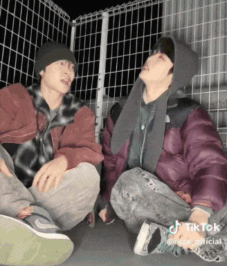 two men are sitting next to each other in front of a fence with tik tok written on the bottom left