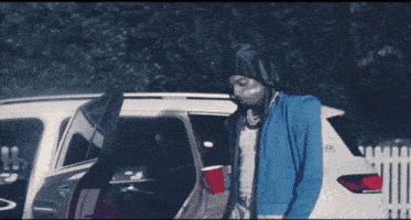 a man in a blue jacket is standing next to a white car with the word hyundai on the back