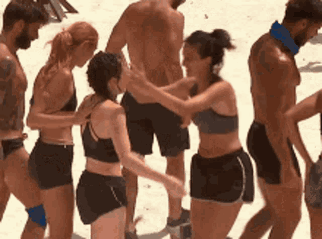 a group of people are standing on a beach and one woman is touching another woman 's neck .