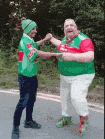 two men in green and red shirts are dancing on a street