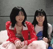 a woman in a red jacket is sitting next to another woman in a white shirt