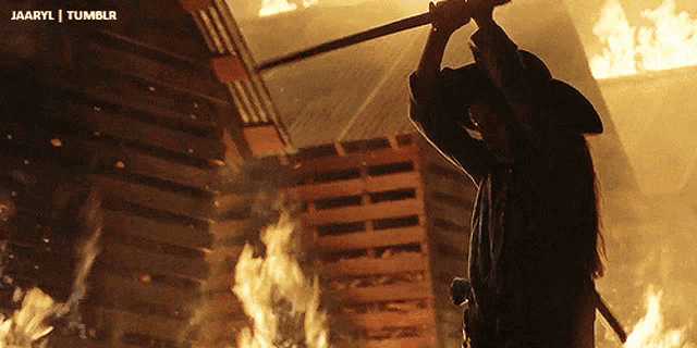 a man in a cowboy hat is holding a sword in front of a burning building
