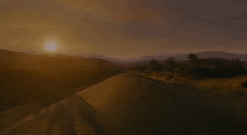 a car is driving down a road at sunset with the sun shining through the clouds .