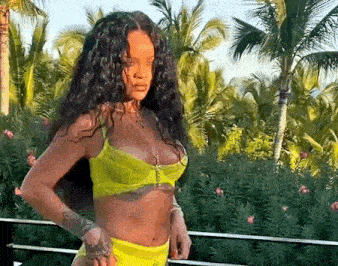 a woman in a yellow bikini is standing on a balcony in front of a palm tree .