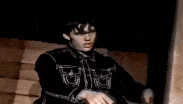 a man in a black jacket is standing in a dark room pointing at something .