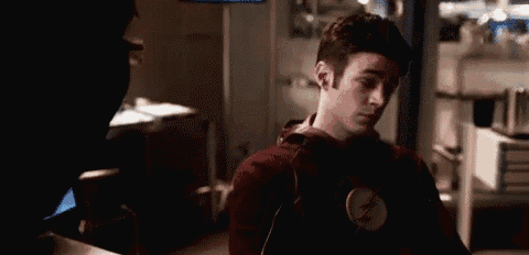 a man in a red sweater with a flash logo on his chest is standing in a dark room .