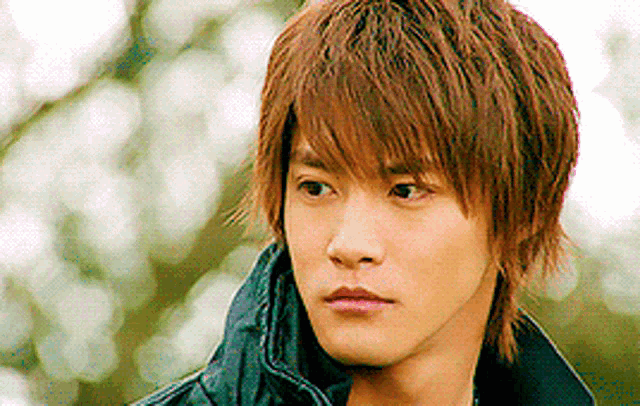 a young man with brown hair is wearing a black jacket and a black scarf around his neck .