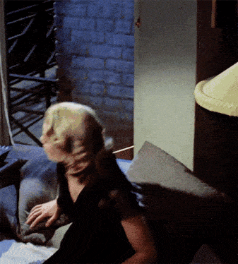 a woman in a black dress is sitting on a couch in front of a brick wall