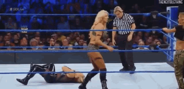two women are wrestling in a wrestling ring with a referee standing behind them .