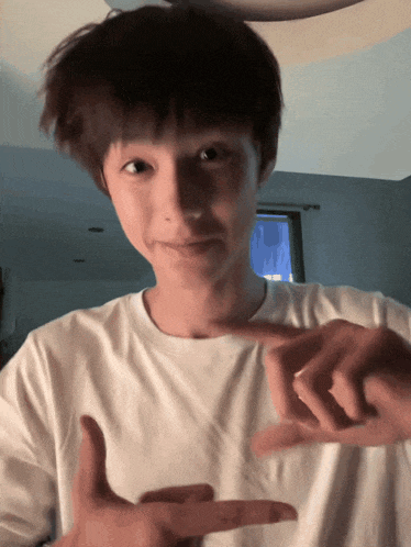 a boy in a white shirt is making a peace sign with his hands