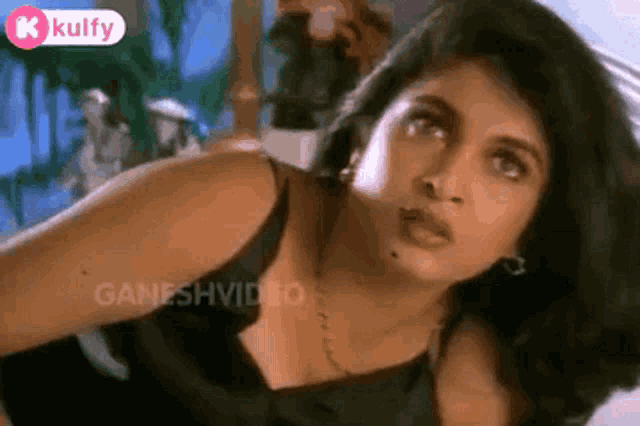 a woman in a black tank top and a necklace is looking up .