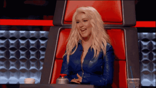 a woman in a blue leather jacket is sitting in a red chair with a drink in her hand .