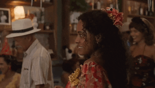 a woman in a red dress with a flower in her hair is dancing in a bar with a man in a white hat .