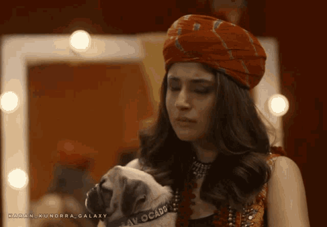 a woman in a turban is holding a small dog with a collar that says av ocado