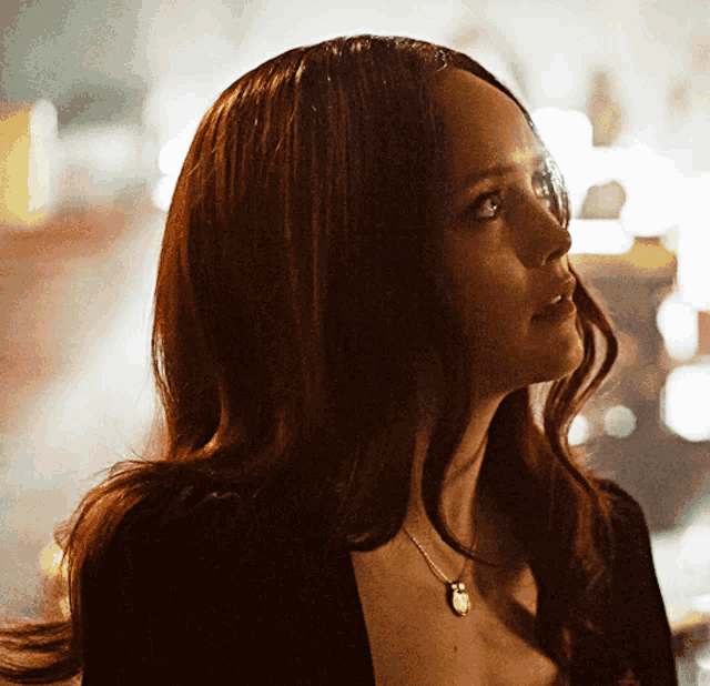 a woman with long red hair is wearing a black top and a necklace