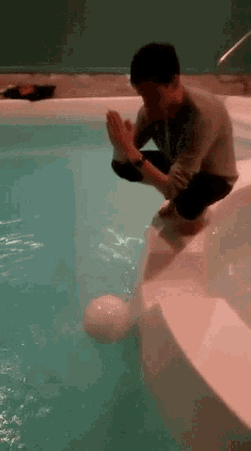 a man is squatting on the edge of a swimming pool with his hands folded