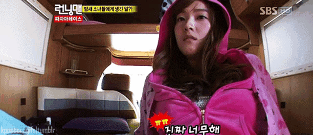 a woman in a pink jacket is standing in a room with a sbs logo on the bottom right