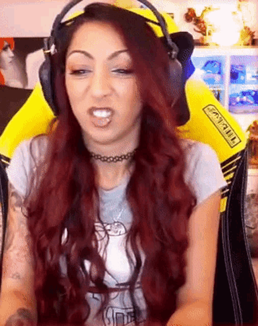 a woman with red hair is wearing headphones and a choker while sitting in a gaming chair that says gigabyte