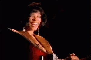 a woman in a gold jacket is smiling while holding a red guitar .