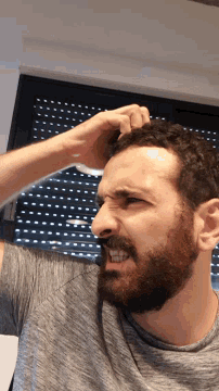 a man with a beard is scratching his head while wearing a grey shirt