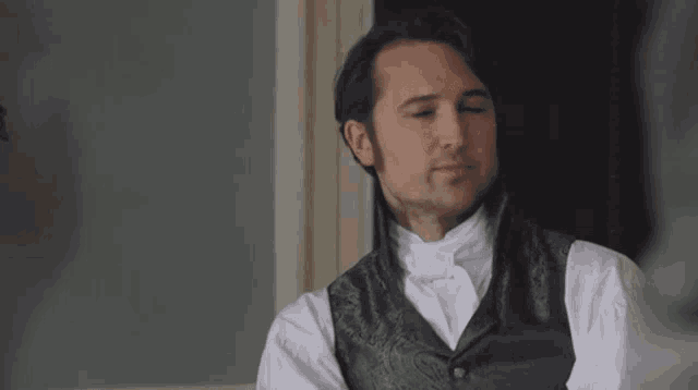 a man wearing a black vest and white shirt is sitting on a couch .