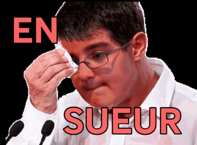 a man with glasses wipes his face with a napkin in front of microphones with the word sueur above him