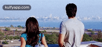 a man and a woman are sitting on a rooftop looking out over the ocean