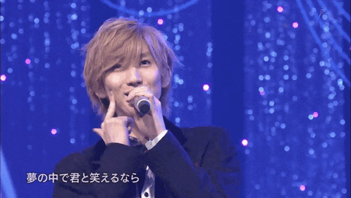 a man in a suit is singing into a microphone with chinese writing on the bottom