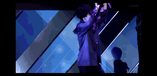 a man in a purple jacket stands on a stage with a microphone in his hand