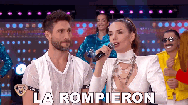 a woman is singing into a microphone while a man looks on and the words la rompieron are on the screen
