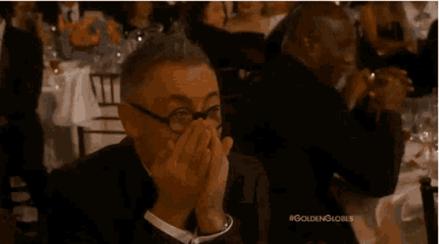 a man in a suit and tie is covering his mouth with his hands at a dinner table .