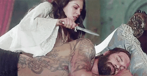 a woman is holding a knife while laying on top of a man .