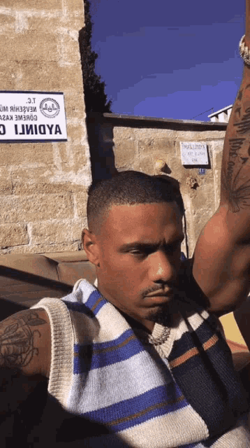 a man with a tattoo on his arm stands in front of a wall with a sign that says ' iiioya '