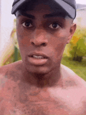 a shirtless man wearing a hat looks at the camera .