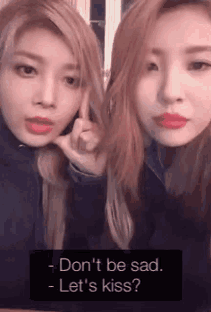 two women are posing for a picture and one of them is saying `` don 't be sad , let 's kiss '' .