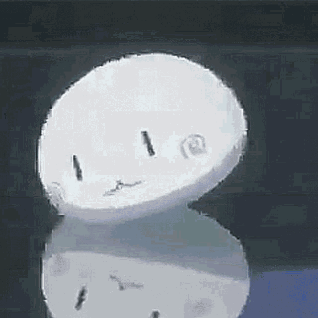 a white circle with a face drawn on it is sitting on top of a black surface .