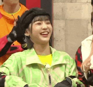 a woman wearing a green jacket and a black hat is smiling and laughing .