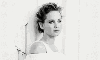 a black and white photo of a woman in a white dress standing in front of a white wall .