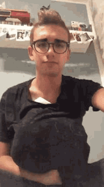 a young man wearing glasses and a black shirt is taking a selfie with his shirt off .